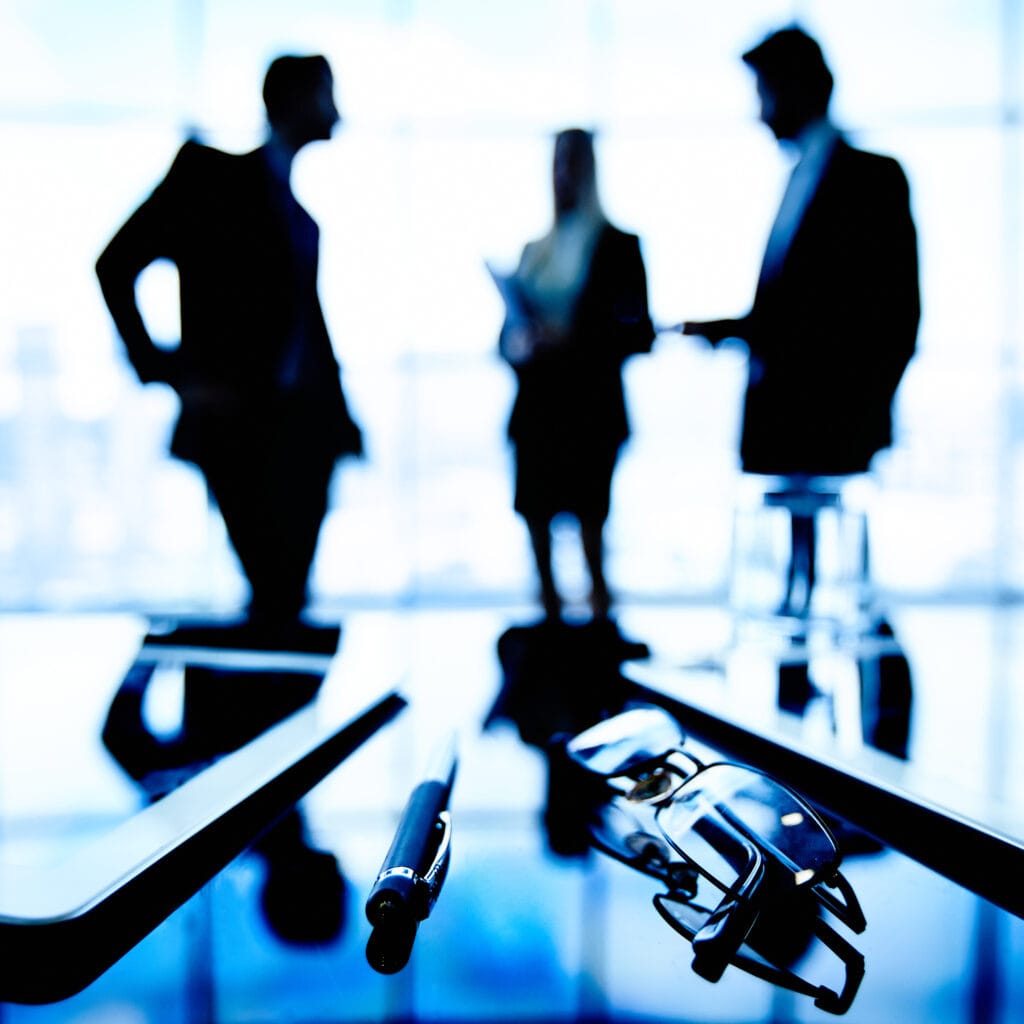 Investors Image of eyeglasses, touchpads and pen at workplace with group of businesspeople communicating on the background